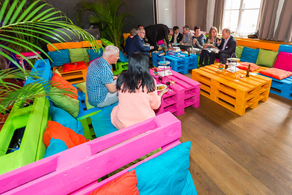 Gäste sitzen auf bunten Palettenmöbeln und geniessen den 40-Jahre-Jubiläumsevent von oetterlidruck.ch im Gespräch.